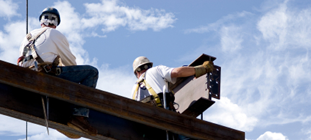 Men in hard hats work on steel beams high in the air.